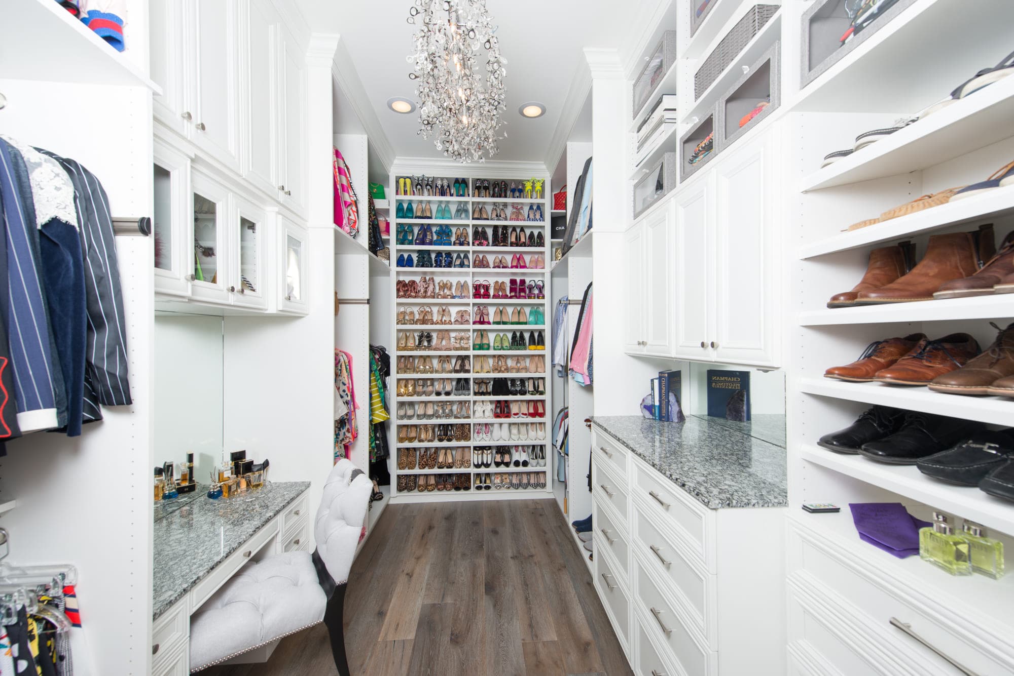 A bright custom walk-in closet with stone counters, a full-height shoe display and a chandelier in a San Diego home.