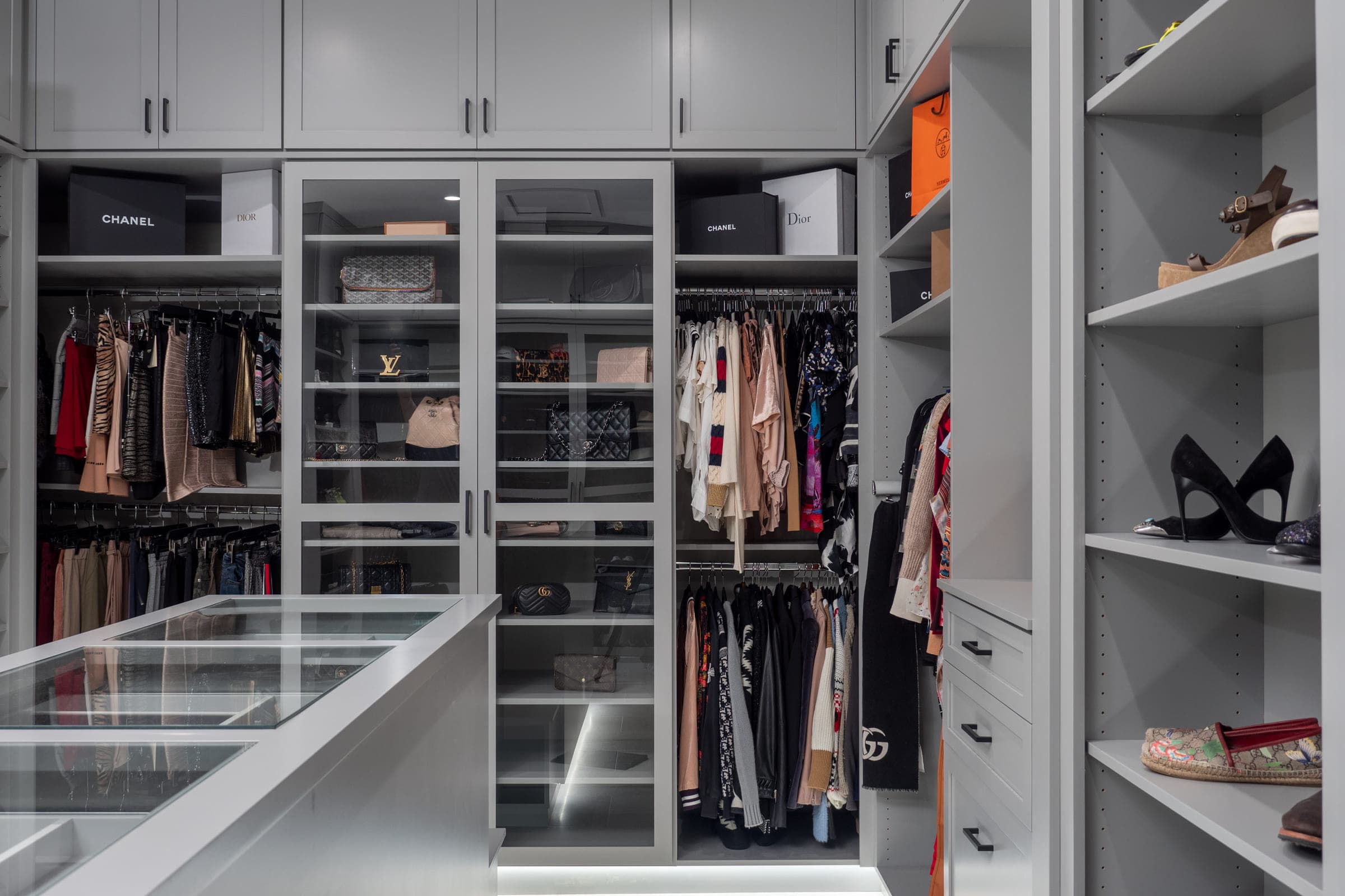 A custom walk-in closet in San Diego with greige cabinetry, glass-front doors and integrated LED-lit shelving.