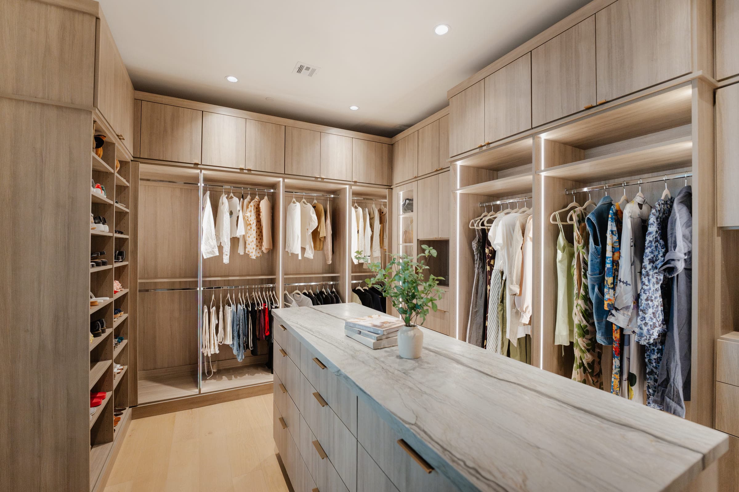 A custom walk-in closet in San Diego with light oak cabinetry, integrated lighting and a marble-topped island, built by Classy Closets.